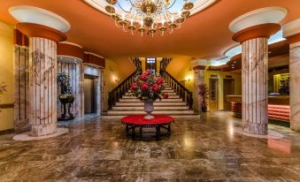 a grand staircase with a chandelier , marble floors , and red furniture in a grand lobby at Zodiaco