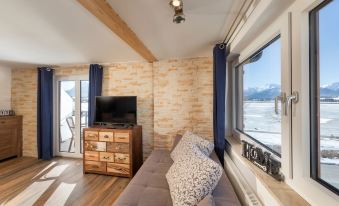 a living room with a couch , tv , and dresser is shown next to a window overlooking the snowy mountains at Hotel Haus am See
