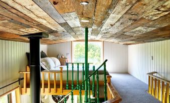 a wooden ceiling with exposed beams , beams extending from the ceiling , and a green handrail on the balcony at Extraordinary Huts