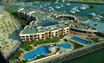 a luxurious hotel complex with multiple buildings , swimming pools , and boats in the marina , all surrounded by trees and buildings at Marina Hotel