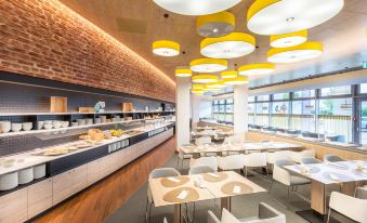 a modern dining area with yellow lights hanging from the ceiling , creating a warm and inviting atmosphere at Hey Lou Hotel Frankfurt Airport
