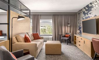 a modern living room with a beige couch , wooden coffee table , and large windows , decorated with gray curtains and orange cushions at Doubletree by Hilton Columbus Dublin