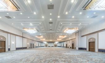 a large , empty banquet hall with high ceilings and multiple rows of seating , under the direction of the esteemed group and provided by the new york at Hilton Memphis