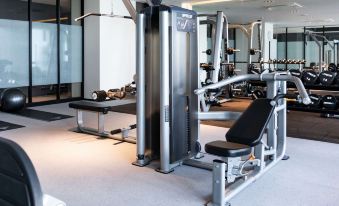 a well - equipped gym with various exercise equipment , including a weight bench and a treadmill , in a well - lit room at Oakwood Suites Yokohama