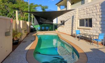 a small , oval - shaped pool is surrounded by a brick patio and chairs , with a house in the background at Best Western Caboolture Gateway Motel