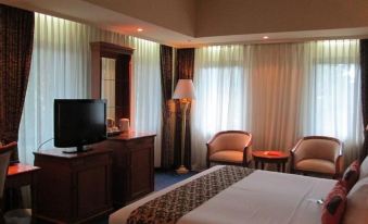 a hotel room with a bed , couch , and tv , as well as curtains and a lamp at Grand Elty Singgasana Hotel