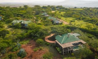 a group of houses with green roofs are nestled in a forested area , surrounded by trees and hills at Ngorongoro Oldeani Mountain Lodge