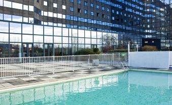 an outdoor swimming pool surrounded by a hotel , with a view of the surrounding buildings at Novotel Marne la Vallee Noisy le Grand Hotel