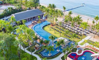aerial view of a resort with a large pool surrounded by palm trees and a beach in the background at La Vela Khao Lak