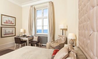 a well - appointed hotel room with a comfortable bed , a desk , a chair , and a window overlooking the ocean at Grand Hotel Heiligendamm - the Leading Hotels of the World