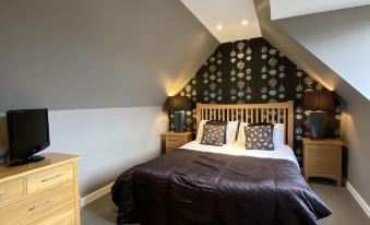 a bedroom with a slanted ceiling and a bed in the center , surrounded by various pieces of furniture at New Inn Hotel