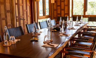 a long wooden dining table with chairs , set for a formal dinner , in a room with wooden walls and large windows at Soneva Kiri