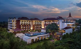 a large , modern hotel building with multiple floors and balconies , surrounded by lush greenery and trees at night at DoubleTree by Hilton Goa - Panaji