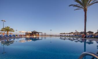 a large outdoor swimming pool surrounded by lounge chairs and umbrellas , with the ocean visible in the background at Vik Gran Hotel Costa del Sol