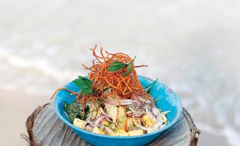 a blue bowl filled with a variety of vegetables and topped with a curly carrot at Pousada Praia Dos Carneiros