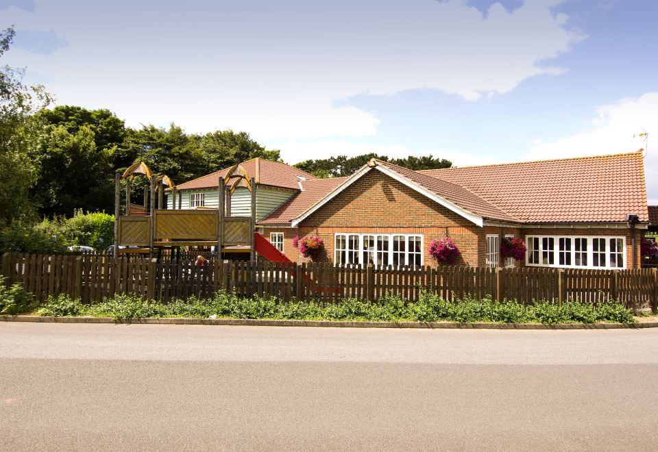 a wooden house with a red roof is surrounded by trees and flowers , along with a fence and flowers at Premier Inn Dover East