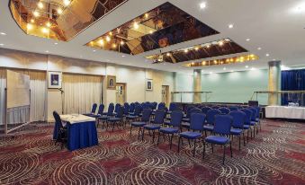 a large conference room with rows of blue chairs arranged in a semicircle , and a podium at the front of the room at Mercure Maitland Monte Pio