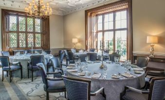 a large dining room with multiple tables set for a formal event , surrounded by elegant chairs and chandeliers at De Vere Latimer Estate