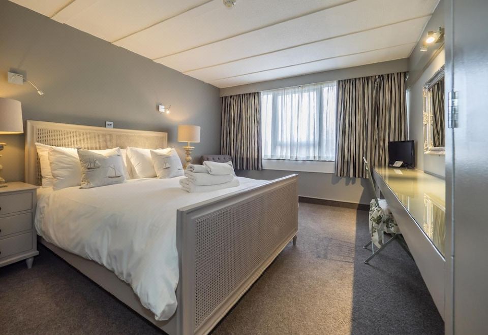 a large , well - made bed is the focal point of a modern hotel room with gray walls and window curtains at Hotel Wroxham