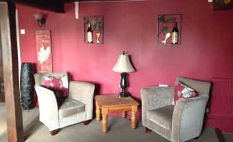 a cozy living room with two grey chairs and a wooden coffee table , surrounded by red walls at The Babbling Brook