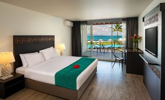 a bedroom with a large bed , a balcony overlooking the ocean , and a dining table at The Pearl South Pacific Resort