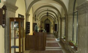 a long , narrow hallway with high ceilings and arched windows , featuring a wooden cabinet and other furniture at Villa Palazzola