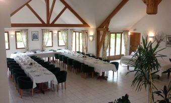 a large dining room with multiple tables set for a formal dinner , surrounded by windows and wooden beams at Logis Hotel Restaurant de l'Abbaye