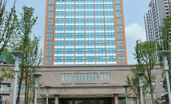 A large building with an entrance to the main parking area in front and another tall skyscraper adjacent to it at Wansheng International Hotel