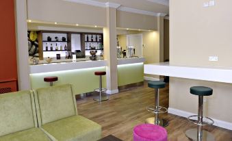 a modern bar area with green chairs , white and pink stools , and a variety of bottles on the shelves at Link Hotel
