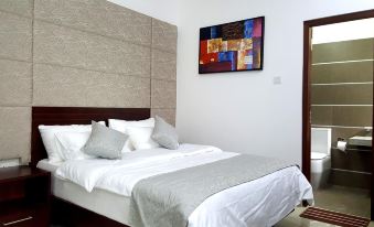 a clean and well - organized bedroom with a white bed , a gray comforter , and a colorful abstract painting on the wall at Click to Go