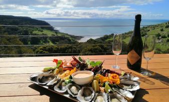 a platter of oysters , an oyster platter , and a bottle of wine are displayed on a wooden table overlooking the ocean at Sea Dragon Kangaroo Island