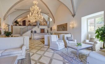 a spacious living room with white walls , large windows , and a grand chandelier hanging from the ceiling at Monastero di Cortona Hotel & Spa
