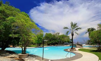 a beautiful swimming pool with palm trees and umbrellas , surrounded by lush greenery under a blue sky at Antulang Beach Resort
