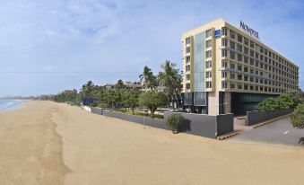 a hotel building with palm trees and a sandy beach in front of it , under a clear blue sky at Novotel Mumbai Juhu Beach