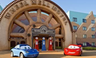 a large , circular building with a wheel - like structure and two blue cars parked in front of it at Disney's Art of Animation Resort