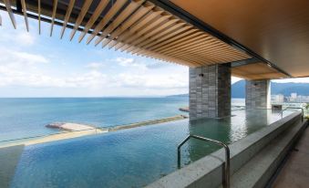 a large outdoor pool surrounded by a wooden deck , with a view of the ocean in the background at Rex Hotel Beppu