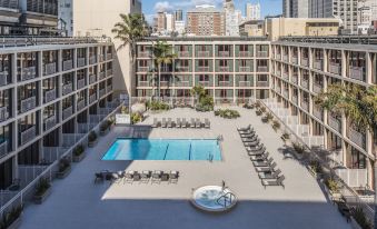 a modern hotel with multiple swimming pools , sun loungers , and umbrellas , surrounded by palm trees and other buildings at Hilton San Francisco Union Square
