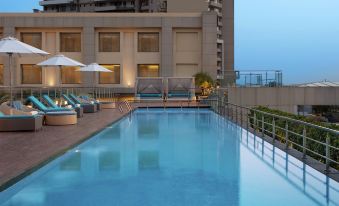 a large outdoor swimming pool surrounded by a building , with lounge chairs and umbrellas placed around the pool area at DoubleTree by Hilton Agra