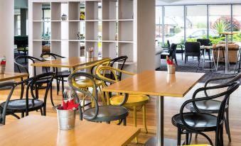 a restaurant with wooden tables and chairs , yellow and black chairs , and a vase of flowers at Ibis Styles Barnsley