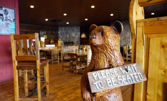 "a wooden bear statue with a sign that says "" please wait to be seated "" in a restaurant" at Daniels Summit Lodge
