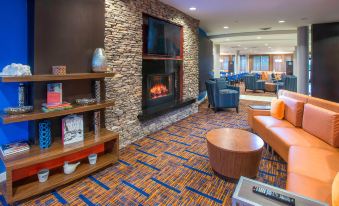 a modern living room with blue carpet , wooden furniture , and a large flat - screen tv mounted on the wall at Courtyard by Marriott Montgomery Prattville