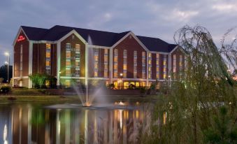 a large hotel building with a fountain in front of it , surrounded by trees and grass at Hilton Garden Inn Jackson/Madison