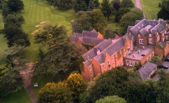 an aerial view of a large , red brick building surrounded by trees and a green field at Coulsdon Manor Hotel and Golf Club