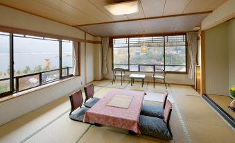 a room with tatami mats on the floor and a table surrounded by chairs , overlooking a lake at Jukeiso