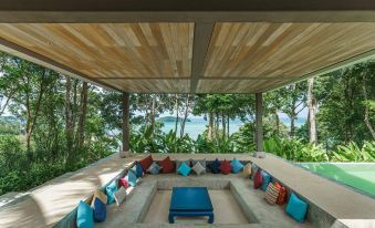 a modern , minimalist outdoor living area with wooden ceiling and blue furniture under a canopy , overlooking the ocean at Island Escape by Burasari