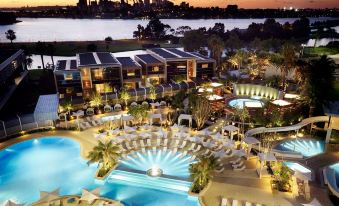 a large resort with a pool and palm trees is shown at dusk , overlooking a city skyline at Crown Metropol Perth