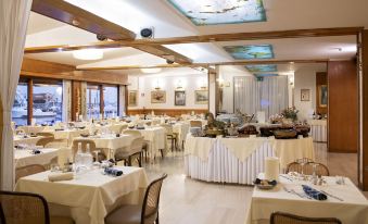 a well - decorated restaurant with multiple dining tables , each set with white tablecloths and chairs , and a ceiling with lights at Hotel L'Approdo