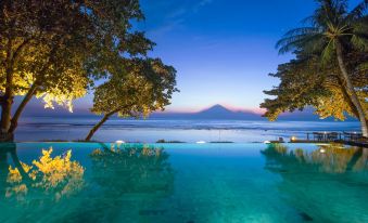 a tranquil swimming pool with a mountain in the background , illuminated by lights at dusk at Jeeva Klui Resort