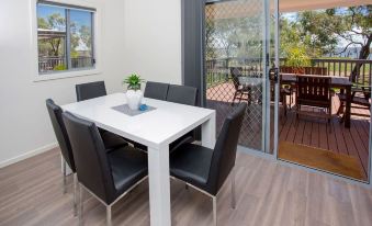 a white dining table with black chairs is set in a room with a sliding glass door leading to an outdoor patio at Discovery Parks - Lake Bonney