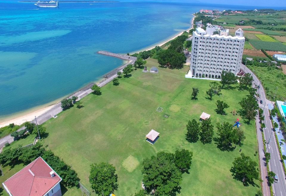 aerial view of a grassy field near the ocean with a large white building in the background at Hotel Royal Marine Palace Ishigakijima
